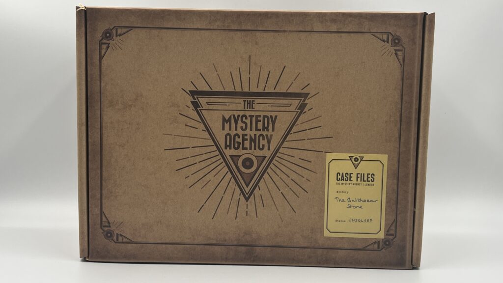 The outer box of The Mystery Agency The Balthazar Stone escape room style game on a plain background. The box shows an unsolved Case Files sticker and The Mystery Agency logo